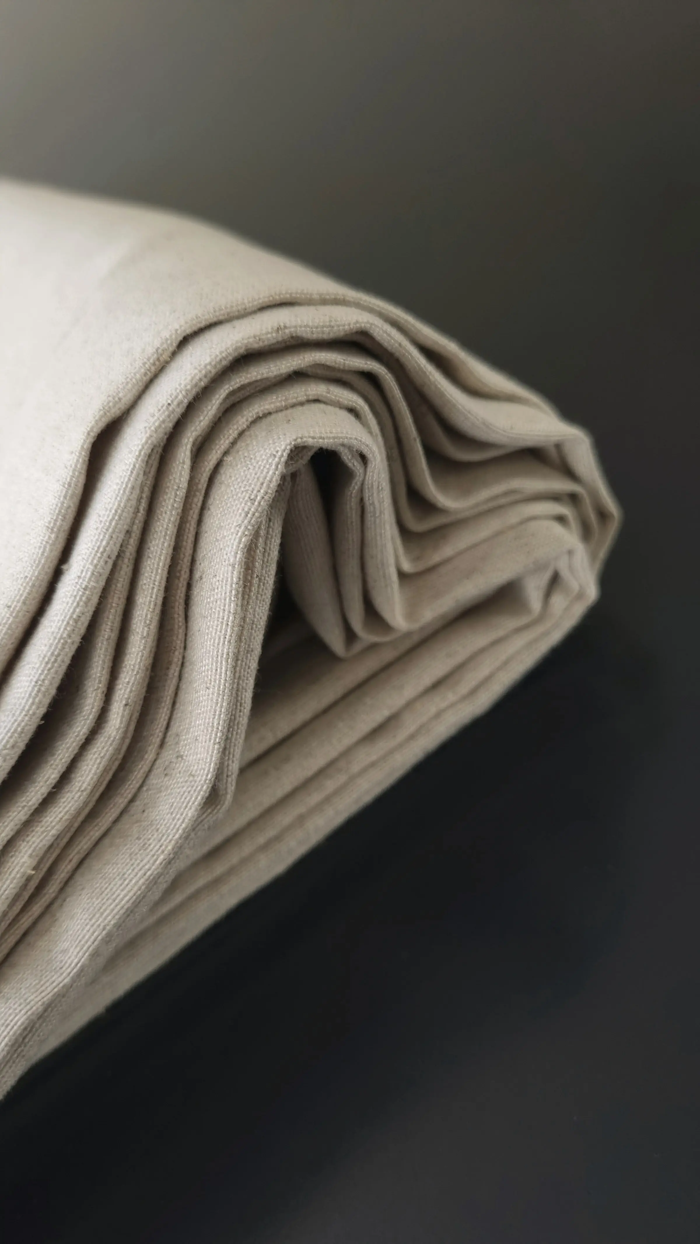 Natural linen folded into a soft stack against a charcoal ground
