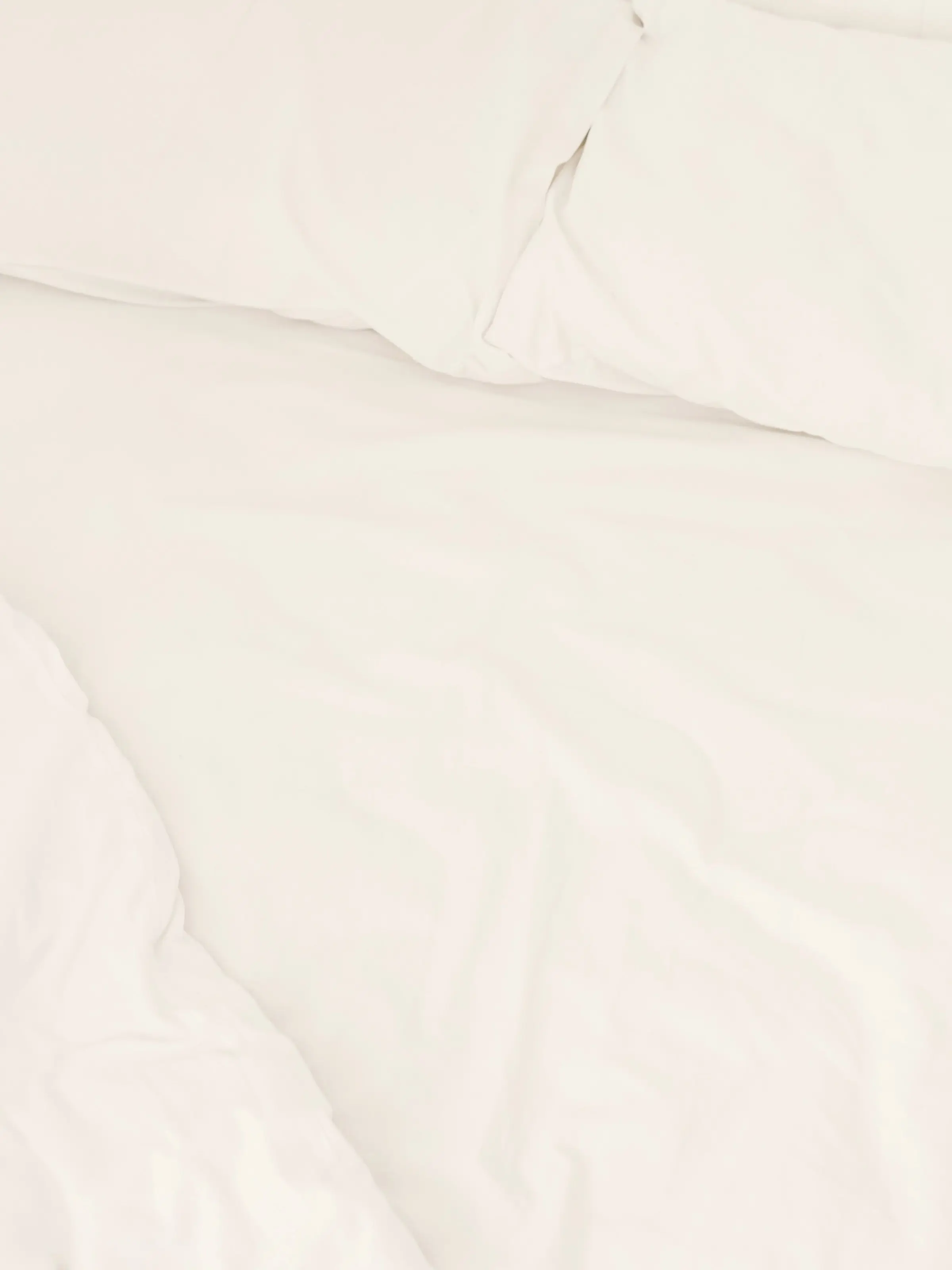 White sheets and pillows on an unmade bed in morning light