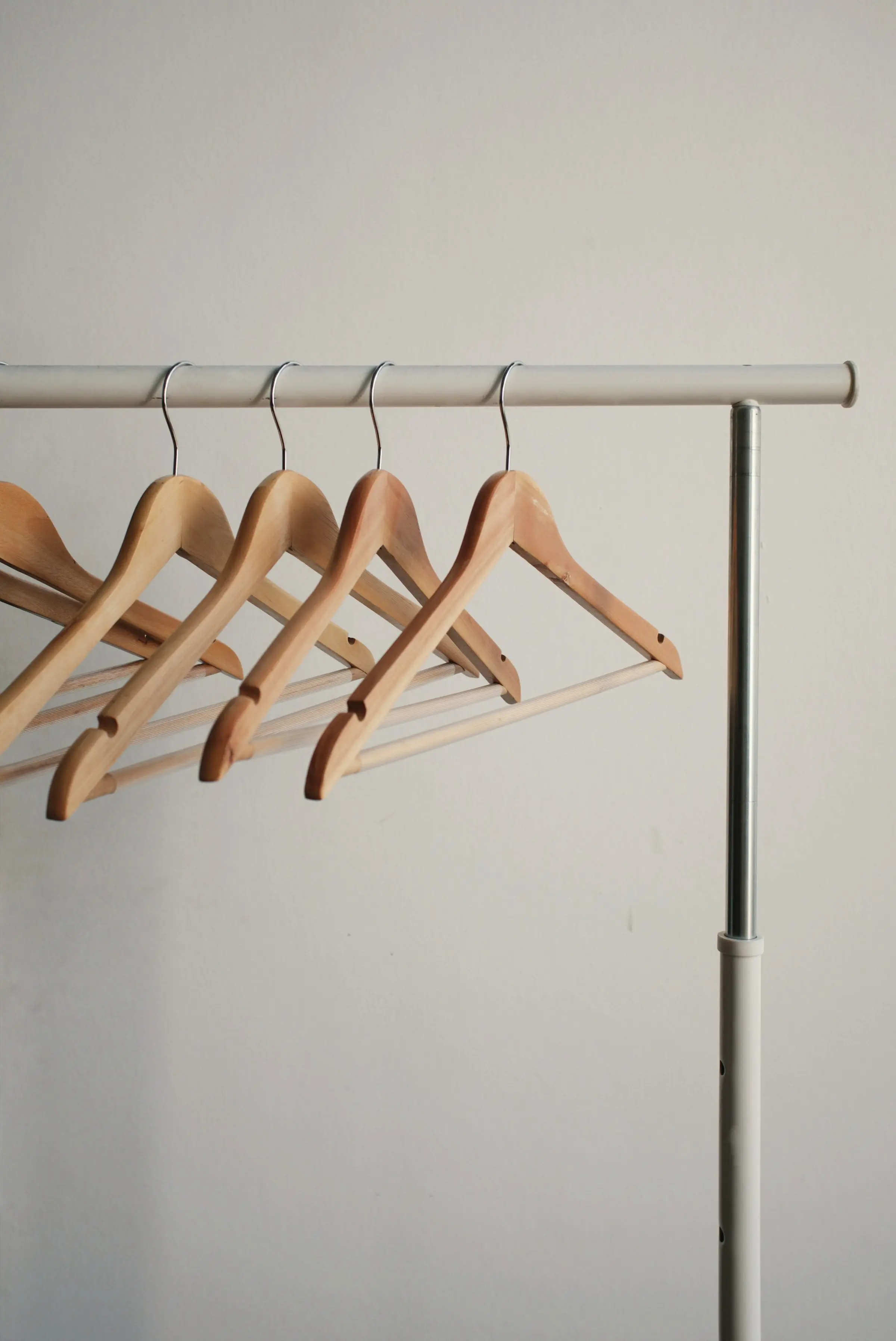 Four wooden hangers on a slim steel rail against a pale wall