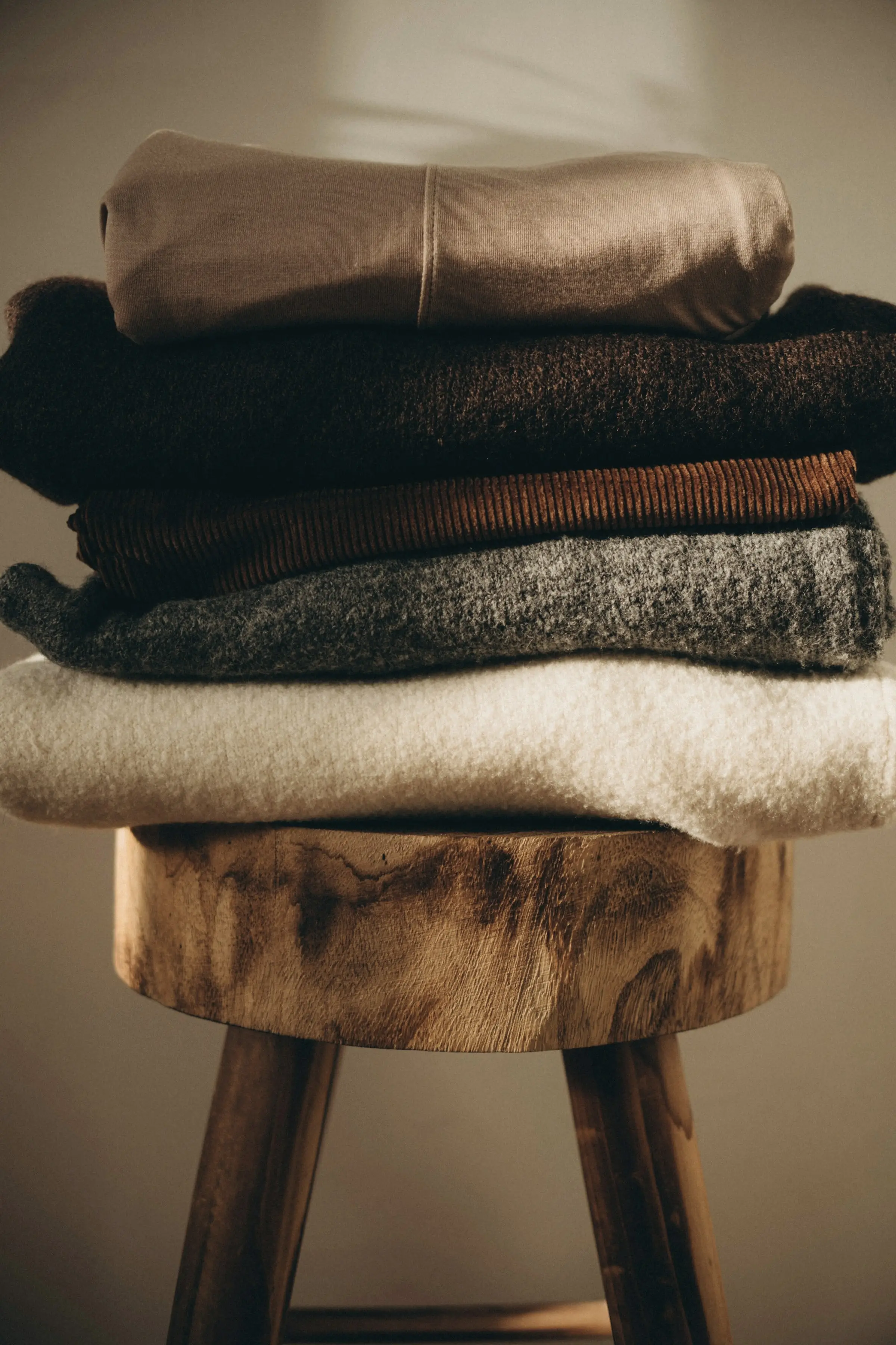 Folded knitwear stacked on a turned wooden stool
